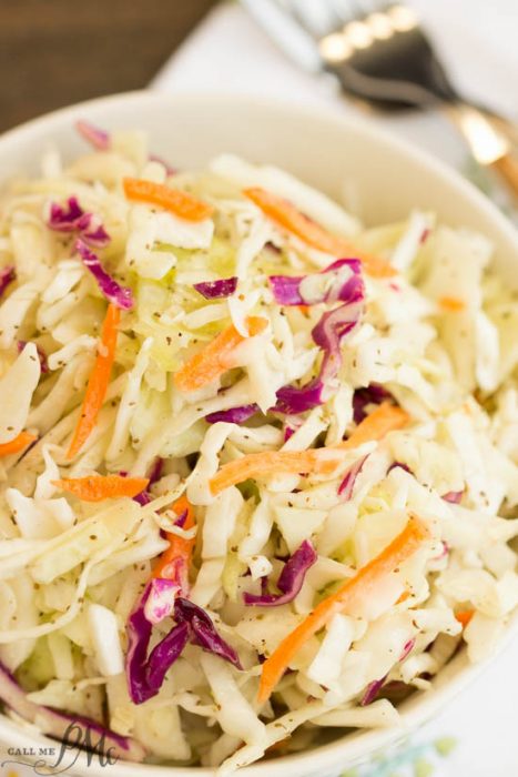 A bowl of Tangy Vinegar Based Slaw with shredded cabbage, carrots, and purple cabbage sits on a white napkin, with a fork in the background.