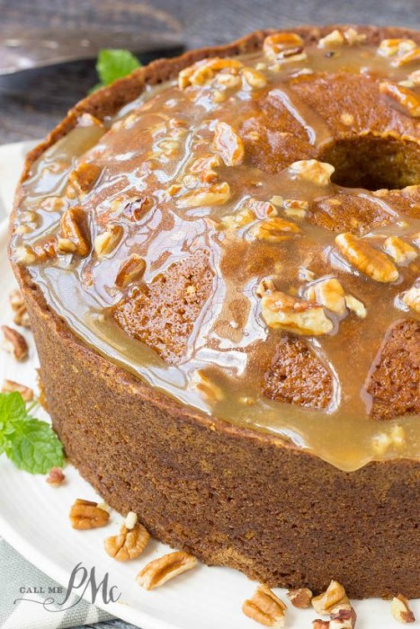 Fantastic fall cake, this Praline Glazed Pumpkin Pound Cake is always a hit! Pumpkin Pound Cake Bundt topped with caramel glaze and chopped pecans, displayed on a white plate with a sprig of mint and scattered pecan pieces.