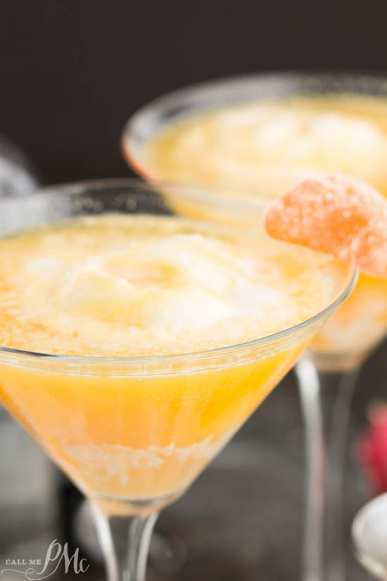 A close-up of a yellow-orange frozen Dreamsicle Martini, served in a martini glass with a sugared orange slice on the rim. Another glass featuring this refreshing Dreamsicle Martini Recipe sits in the background.