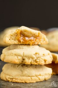 A stack of caramel stuffed sugar cookies with caramel centers, one cookie on top is broken in half, revealing gooey caramel inside.