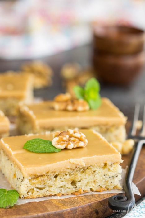 Recipe. Banana bread, blondies, brownies, cake. Moist and dense, Banana Bread Blondies with Quick Caramel Frosting have the texture of brownies and taste like banana bread! This dessert is rich, filling, and sweeter than traditional banana bread. It's a great recipe for brunch or snack with coffee. Another bonus, they are easy to prepare and cook faster than a loaf. A square piece of dessert, topped with a walnut and mint leaf, sits on a wooden board, with more cake pieces and bowls blurred in the background.