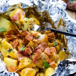 These easy Campfire Potato Foil Packs are flavorful, loaded potatoes cooked inside foil packs, then topped with melty cheese and bacon. This quick, delicious, and nourishing side dish recipe is great while camping or in the oven for any occasion! No pans to wash afterward makes the cook happy too!