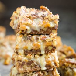 A stack of Pecan Pie Magic Cookie Bars on top of a piece of parchment paper.