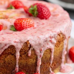 A strawberry cake with icing, strawberries, and cream on a plate.