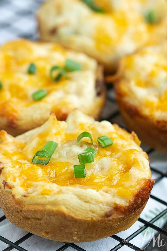 These Baked Crack Chicken Biscuit Bites are full of chicken, ranch, bacon, and cheese in convenient biscuit dough cup. Simple to make and always a crowd-pleaser! This recipe is great for game day, entertaining, and snacks. Close-up of appetizers cups, cheesy bread cups topped with chopped green onions, resting on a wire cooling rack.