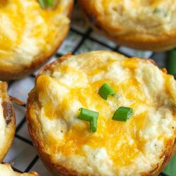Close-up of Crack Chicken Biscuit Bites, cheesy bread cups topped with chopped green onions, resting on a wire cooling rack.