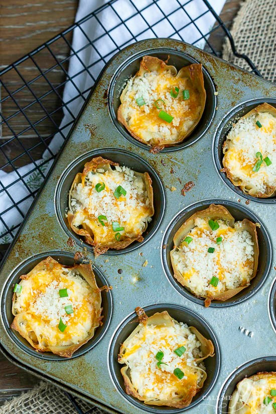 Easy and hearty, Crack Wontons are a two-bite appetizer that's filled with creamy, flavorful Crack Chicken. #chicken #appetizer #bacon Muffin tin with crispy appetizer filled with melted cheese and topped with chopped green onions.