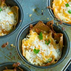 Muffin tin with crispy crack wonton cups filled with melted cheese and topped with chopped green onions.
