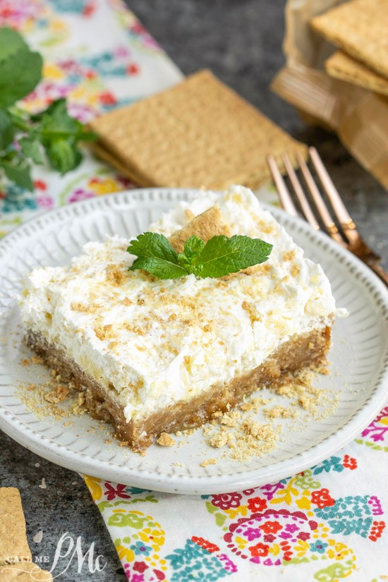 This Hawaiian Pineapple Delight Dessert Recipe is rich but light. It has a graham cracker bottom and a refreshing pineapple spiked whipped topping layer. A creamy Dessert square, topped with a mint leaf and crumbled topping, sits elegantly on a white plate.