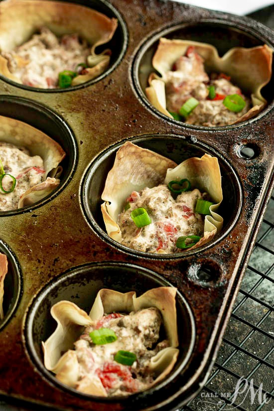 A muffin tin filled with Cream Cheese Sausage Rotel Wonton Cups, each holding a creamy meat and vegetable mixture, garnished with chopped green onions.