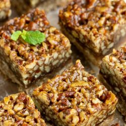 Pecan bars on a baking sheet with a mint sprig.