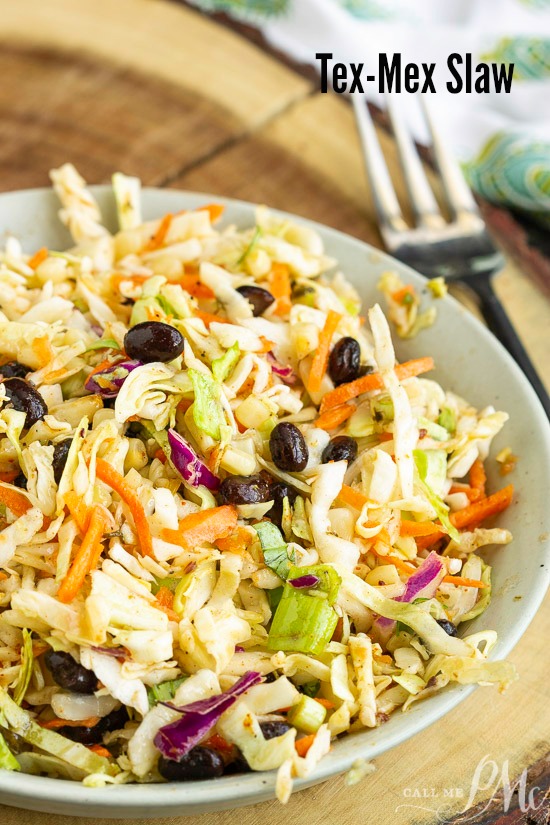 Tex Mex Coleslaw is packed with flavor and perfect for summer cookouts. It also adds a nice crunch to tacos, fajitas, and wraps. #coleslaw #salad #Mexican #TexMex A vibrant slaw sits in a bowl, featuring carrots, black beans, and shredded cabbage on a wooden board. A fork and napkin linger in the background, completing the scene.