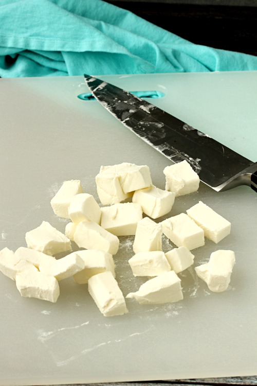 Cream cheese cut into cubes on a cutting board with knife