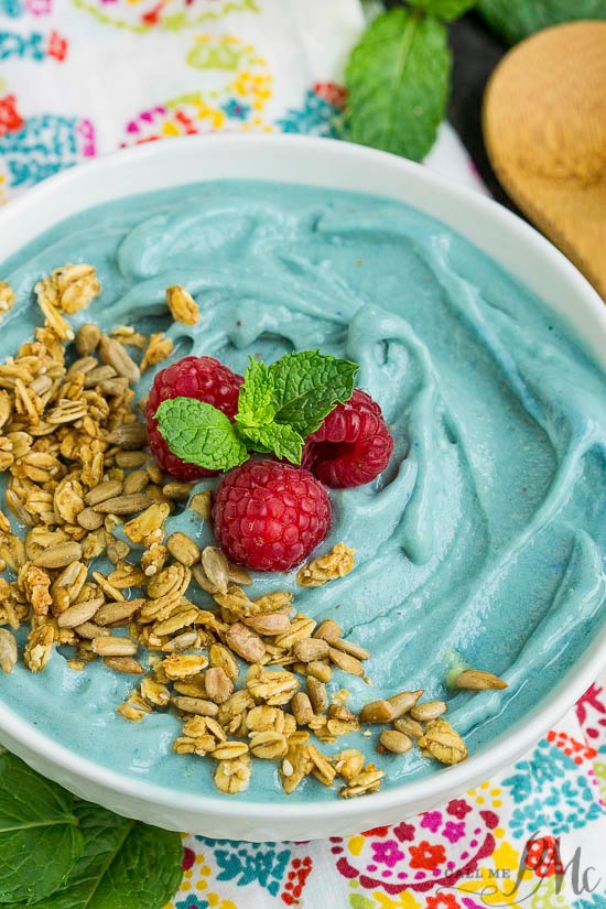 Bowl full of blue smoothie and topped with granola and raspberries.