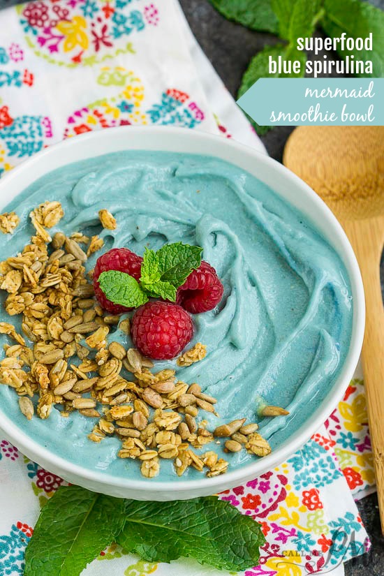 Bowl full of blue smoothie and topped with granola and raspberries.