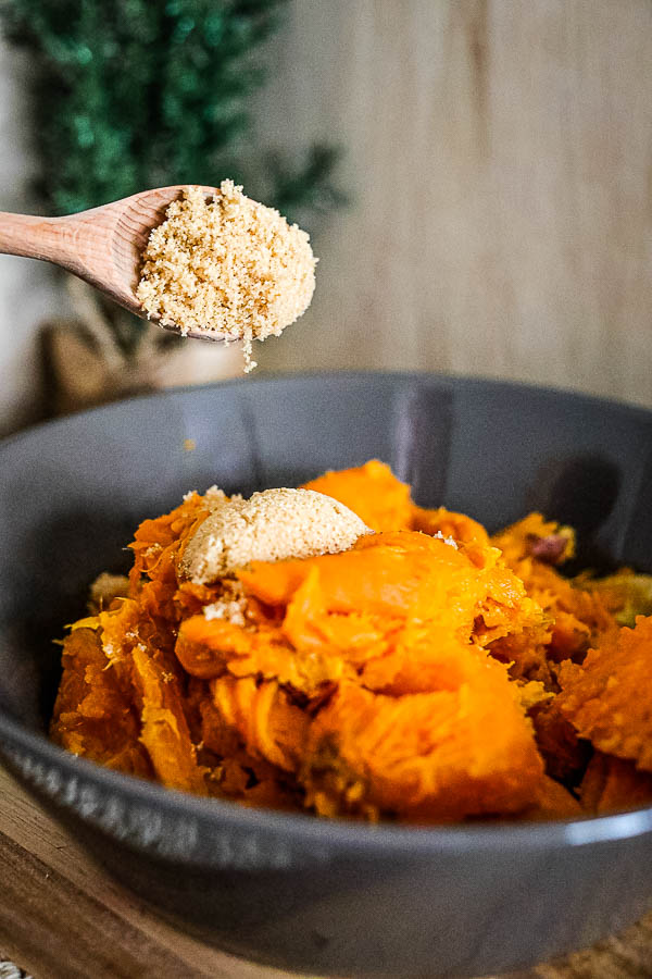 pouring cinnamon butter over sweet potatoes in bowl