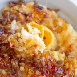 A close-up of mashed plantains topped with crispy pork bits and drizzled with a reddish Captain Rodney's Dip sauce, with a spoonful lifted from the plate.