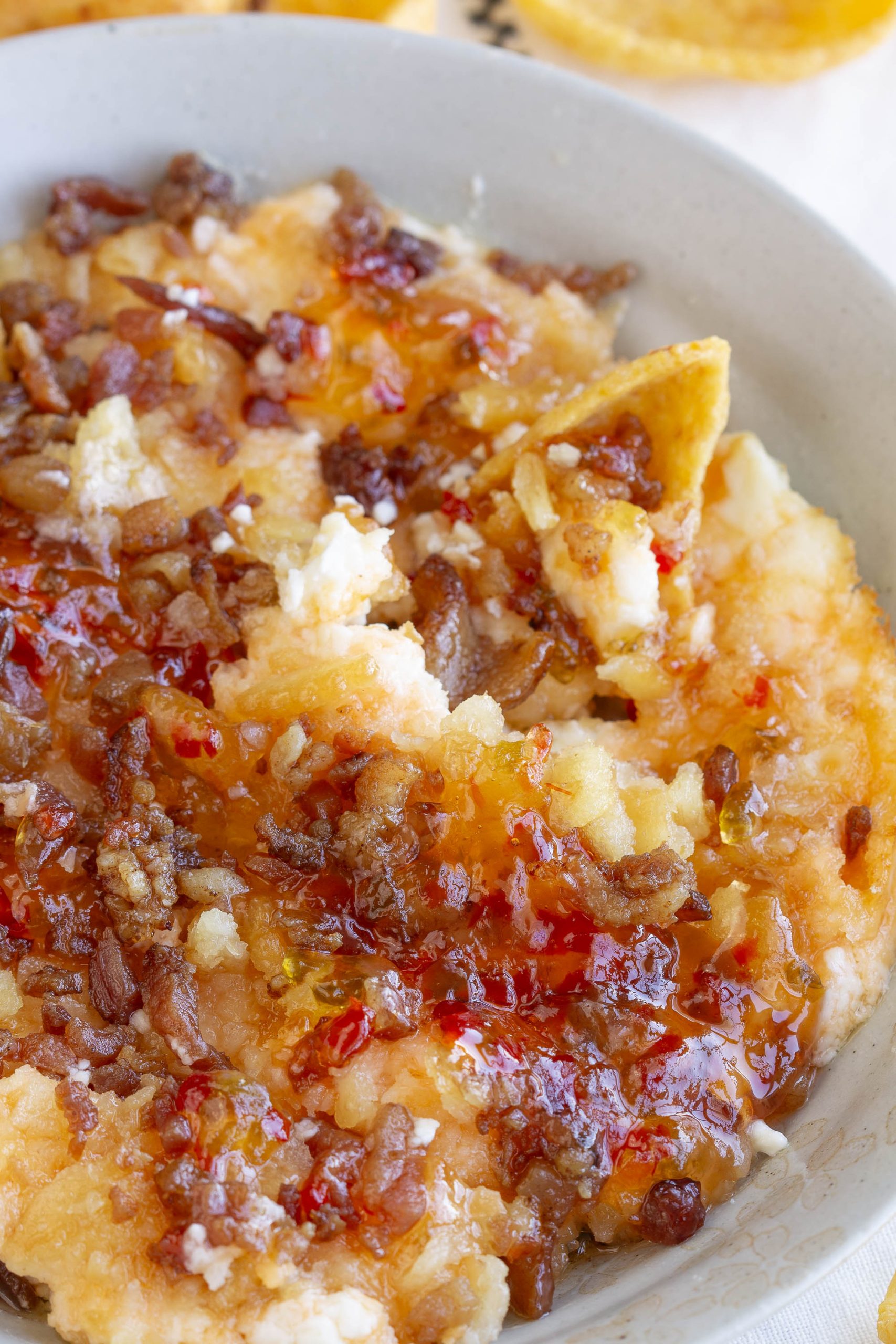 A close-up of a bowl of Captain Rodney's Dip topped with sweet chili sauce and crispy bits, with part of a chip visible dipping into the cheese.
