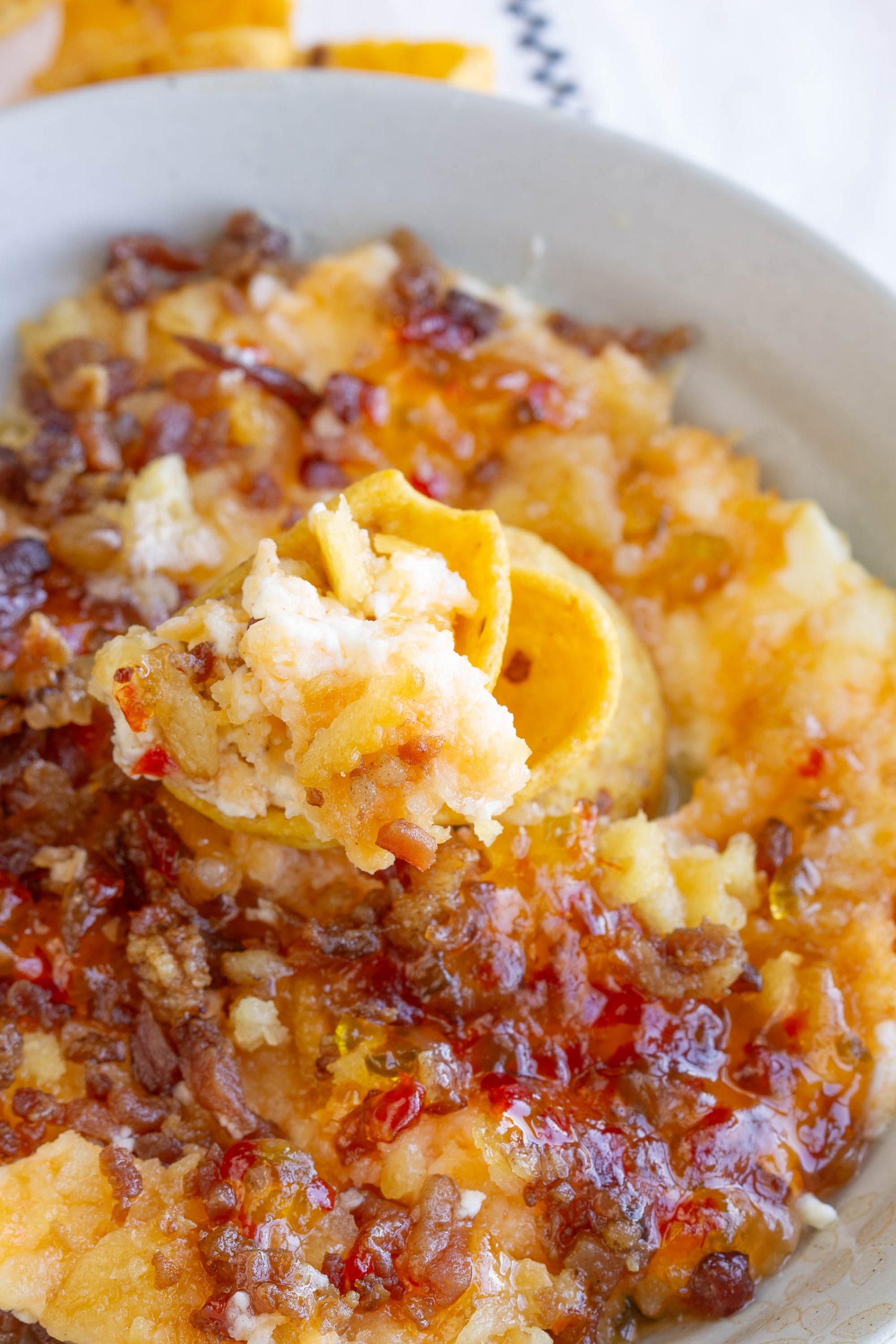 A close-up of mashed plantains topped with crispy pork bits and drizzled with a reddish Captain Rodney's Dip sauce, with a spoonful lifted from the plate.