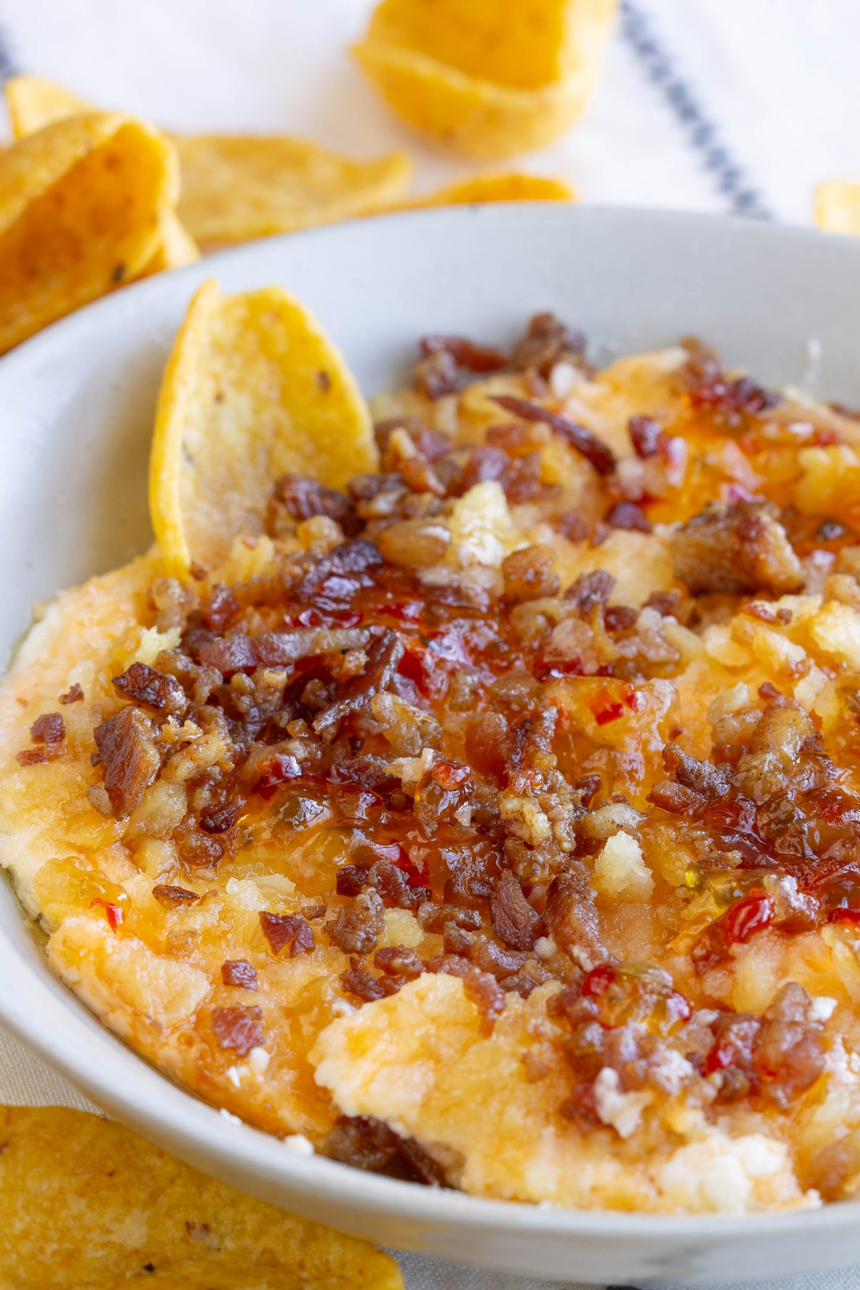 A bowl of cheesy Captain Rodney's Dip topped with bacon bits and served with crispy corn chips.