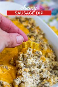 A delicious chip is hand-dipped into a rich and creamy Cheesy Sausage Dip, beautifully presented in a white dish.