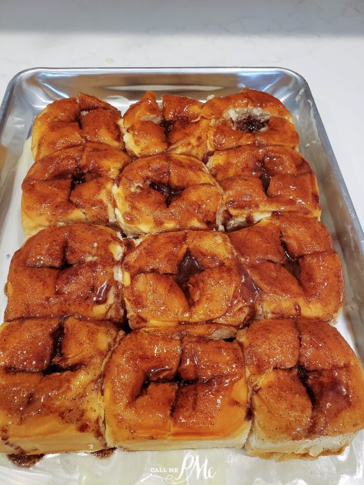 A baking tray of bread, each topped with a glossy layer of cinnamon sugar glaze.