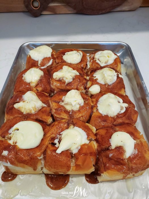 A tray of twelve Quick Cinnamon Hawaiian Rolls topped with dollops of cream cheese icing, arranged neatly on a metal baking sheet.