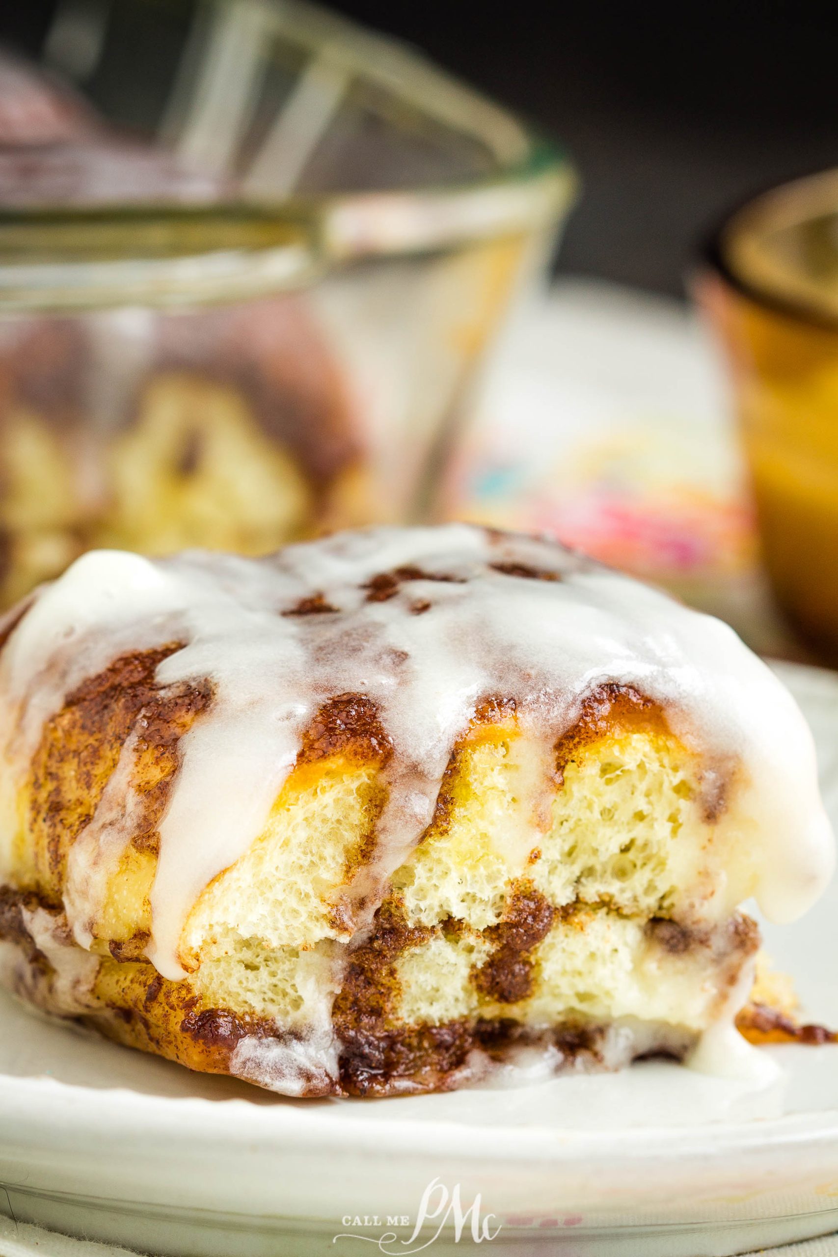 A close-up of breakfast with white icing on top, placed on a white plate with a glass baking dish in the background.