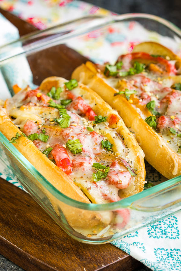 Sausage Pepper Onion Hoagies a delicious, hearty 30-minute meal! Italian sausage, onions, peppers, tomato sauce, and lots of mozzarella make this sandwich a family favorite. #sausage #sandwich #Italian #hoagie #pizza #pizzasandwich #pizzahoagie #pepeprs #onions #Italiansausage #easy #20minute #recipe Buns stuffed with meat and cheese in a casserole dish.