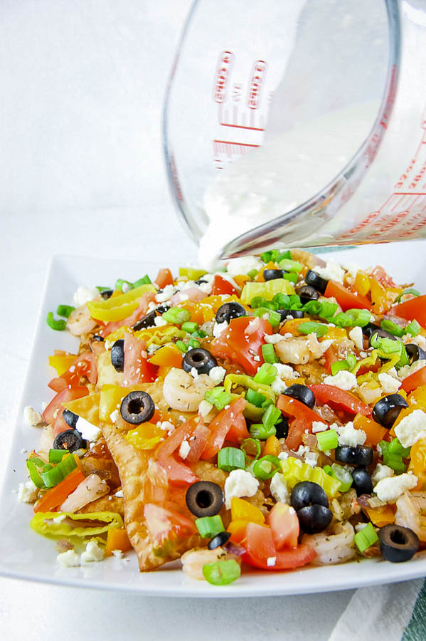 Greek Seafood Nachos are a delicious Mediterranean twist on a snack or dinner recipe. They are a fun and simple dinner solution full of fresh ingredients and flavor! #recipes #Greek #nachos #seafood #shrimp #crawfish #feta #easy #tailgating #party A plate of food with tomatoes and black olives.