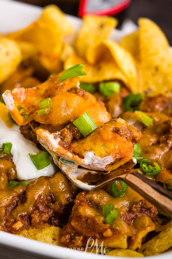 Frito Chili Pie Recipe is classic comfort and gameday food. It's simple, hearty, delicious, takes just minutes to make, and the whole family loves it! #cornchips #Fritos #chips #chili #cheese #cheddar #meal #fastfood #copycat Close-up of food featuring seasoned meat, melted cheese, diced green onions, and a dollop of sour cream on top of corn chips.