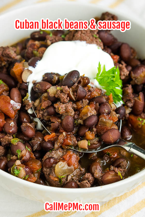 Bowl of cooked black beans with sour cream and garnish Cuban Black Beans and Sausage, if you have a large family or crowd to feed, need a budget-friendly meal, or like to use pantry staples, #recipe #slowcooker #oven #blackbeans #driedblackbeans #sausage #easy #stew #soup #TexMex