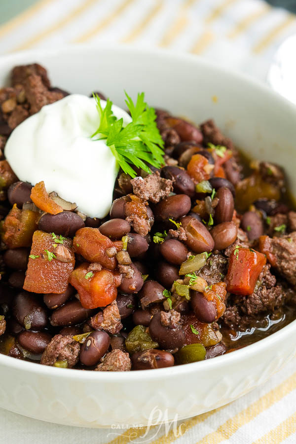bowl of cooked beans, ground beef, tomatoes, and garnish with sour cream A bowl full of meat and vegetables with tomatoes.