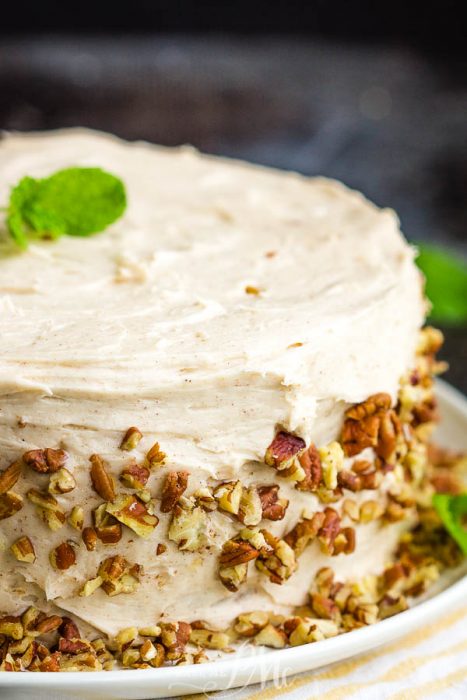 A Gingerbread Layer Cake recipe featuring a frosted cake garnished with chopped pecans on the sides and topped with a sprig of mint, beautifully displayed on a white plate.