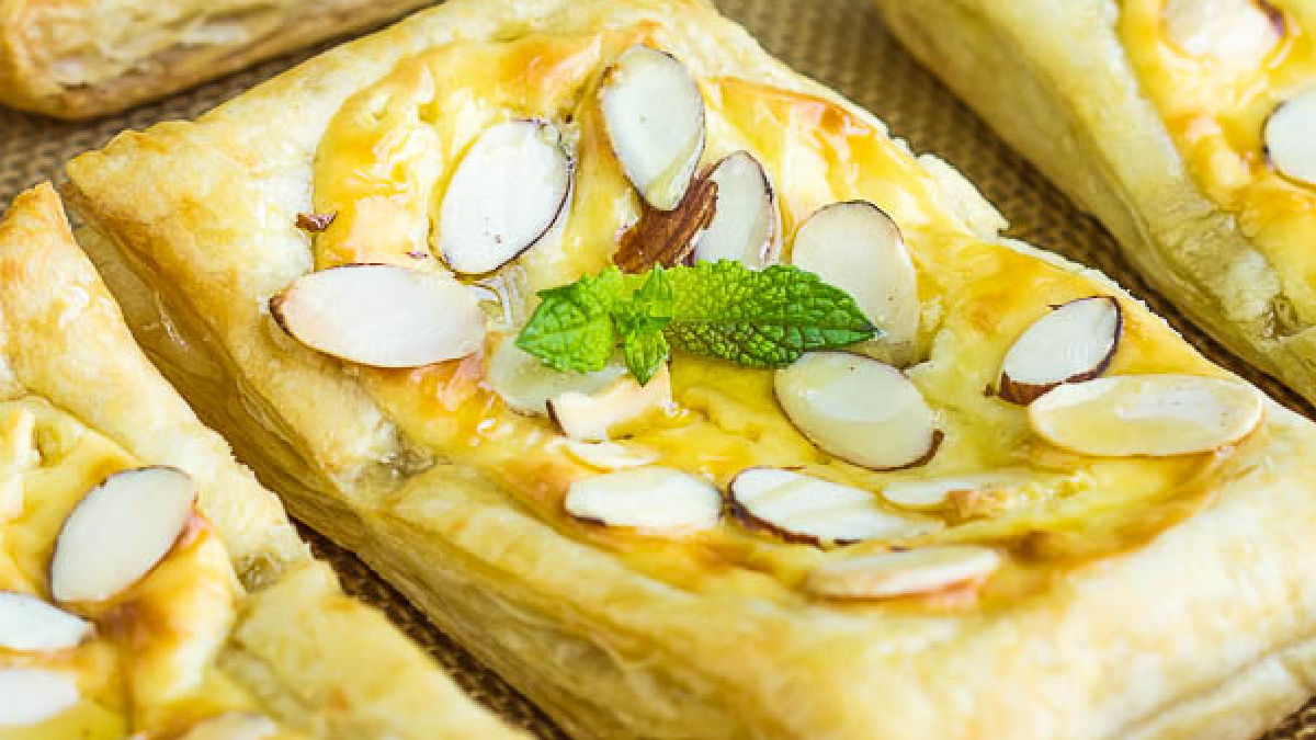 Rectangular Almond Puff Pastry Danish topped with sliced almonds, a creamy filling, and a small sprig of fresh mint in the center, arranged on a textured surface.