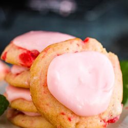 Frosted Amish Cherry Sugar Cookies are crispy around the edges yet pillowy soft and chewy inside. They get their pink color, great flavor, and soft texture from maraschino cherries. #cookies #cherrycookies #shirleytemple #shirleytemplecookies #homemade #recipes #dessert #Christmascookies