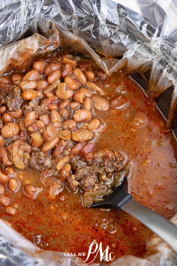 Cooked beans and sausage in a slow cooker with a spoon A bowl of beans with pieces of vegetables, garnished with chopped herbs.