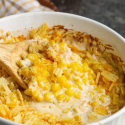 Cheesy creamy corn casserole in a white dish with a wooden spoon.