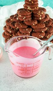measuring cup of pink cookie frosting next to a cookie tower.