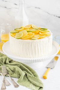 This cake is bursting with layers of bright summer citrus flavor. This cake mix cake tastes like a fancy bakery cake from the addition of sour cream, pudding, and Jello. Topped with luscious buttercream and lemon, lime, and orange slices, this Citrus Cake is perfect for spring!