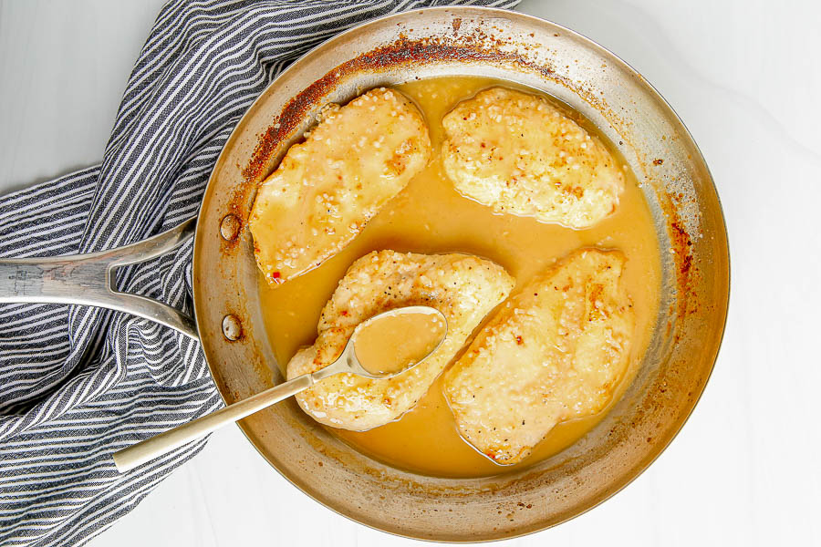 Four chicken cutlets in a sauce pan with gravy.