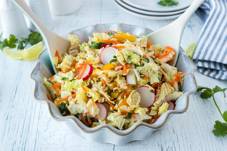 A serving bowl filled with Napa Cabbage Slaw with two serving spoons.