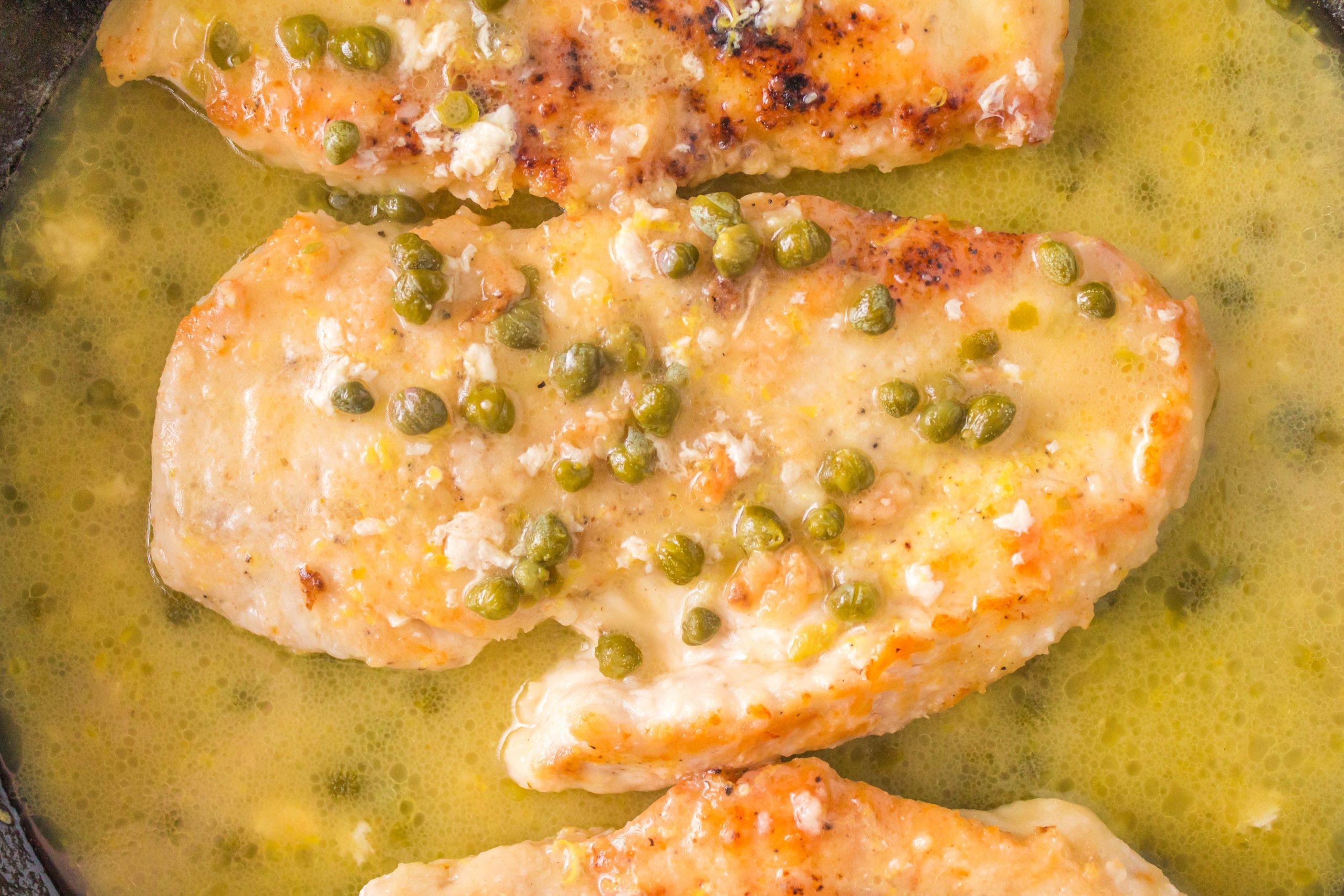 One chicken cutlet in saucepan with capers and butter.