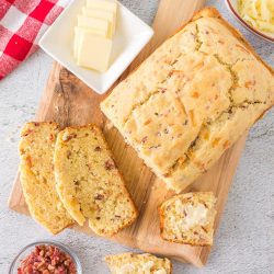 A quick bread with cheddar cheese and bacon on a cutting board.