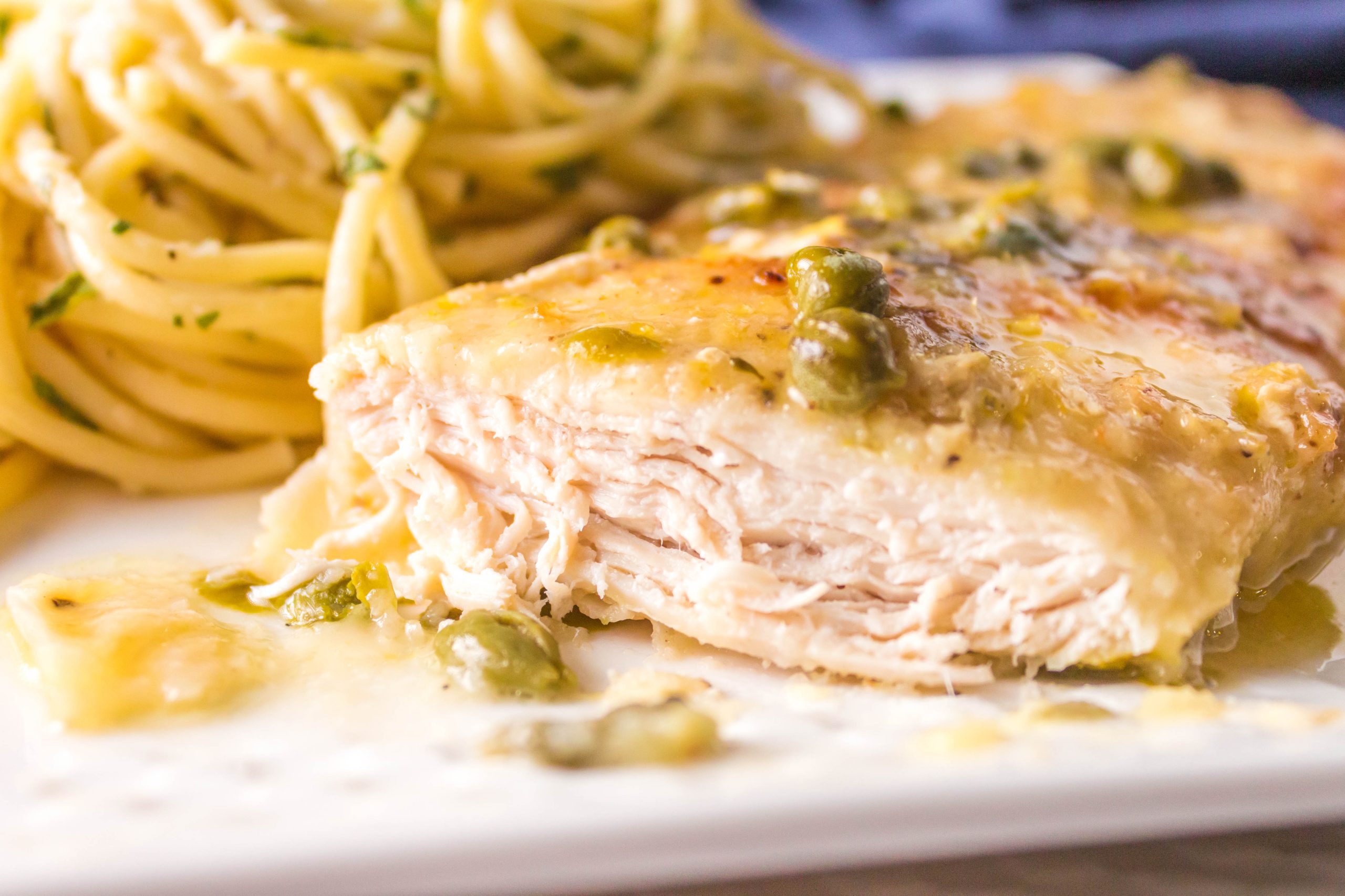 Chicken Piccata Pasta Chicken breast cut with pasta in the background.