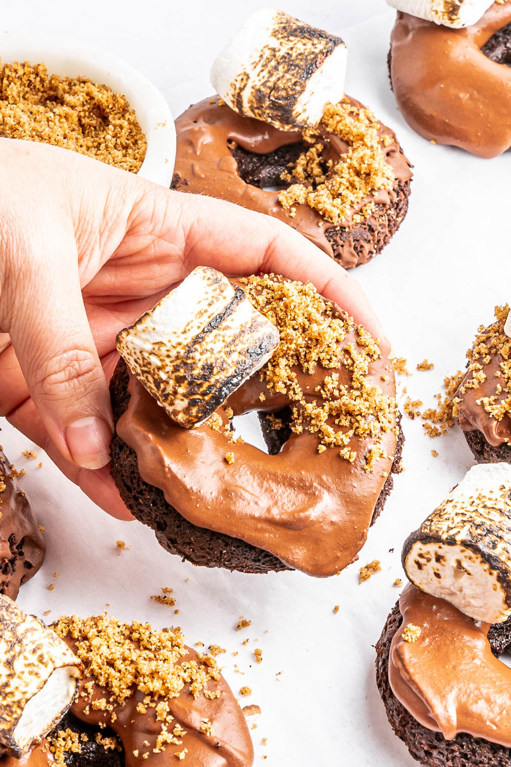 The delicious S'mores Doughnuts Recipe starts with a quick mix, then baked, and topped with a chocolate glaze, a toasted marshmallow, and crushed graham crackers. They are soft, sweet, and decadent.