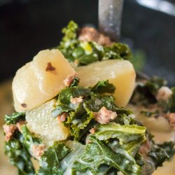 Slow Cooker Zuppa Toscana with a spoonful of kale and potatoes.