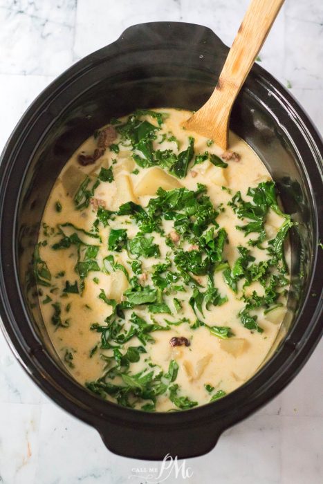 A crock pot of soup with vegetables and a wooden spoon.