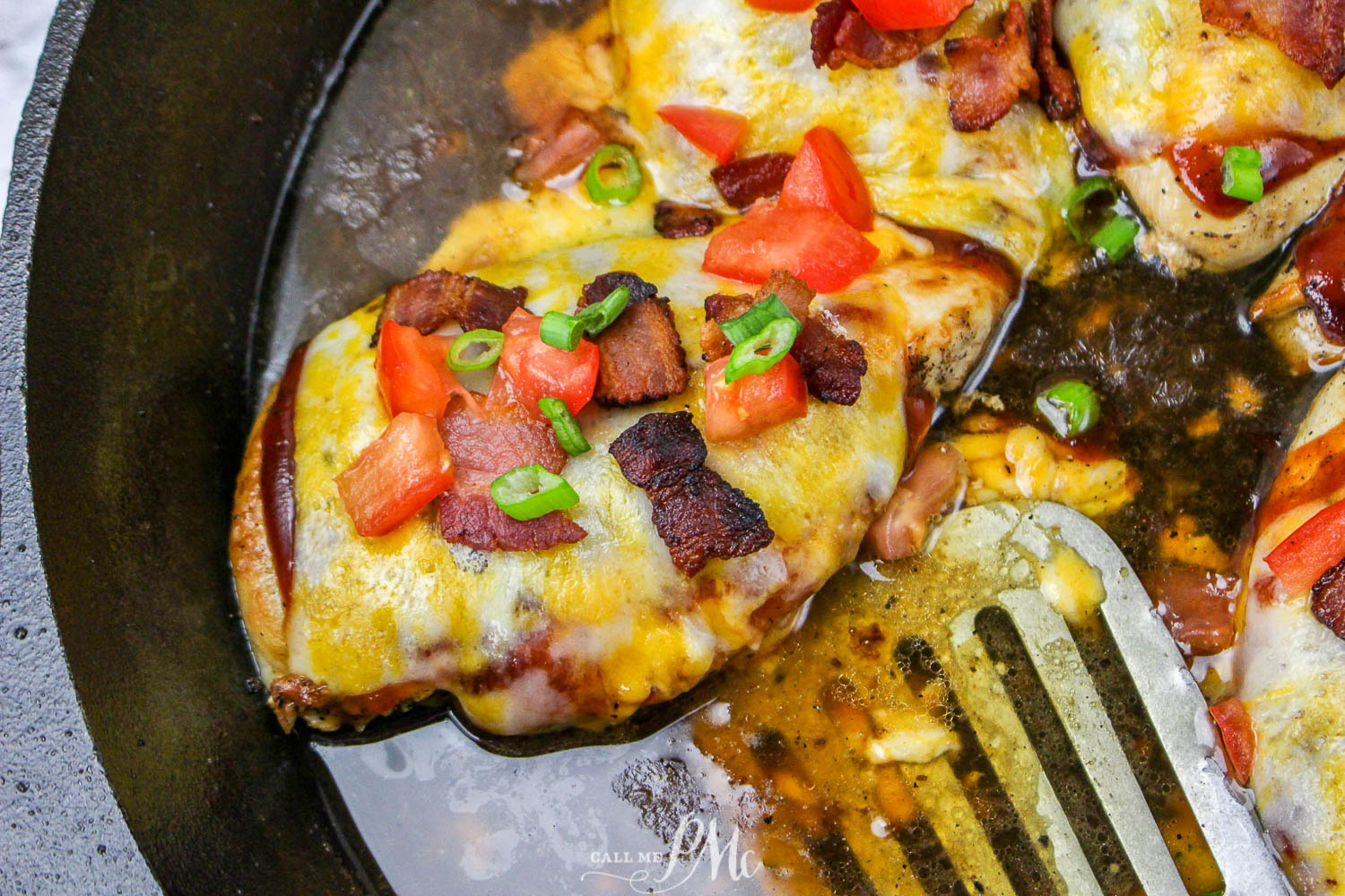 Cheese covered chicken in a skillet with a spatula.