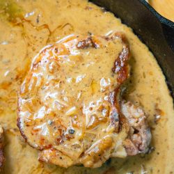A peppercorn pork chop with creamy onion gravy sizzles perfectly in a cast iron skillet.